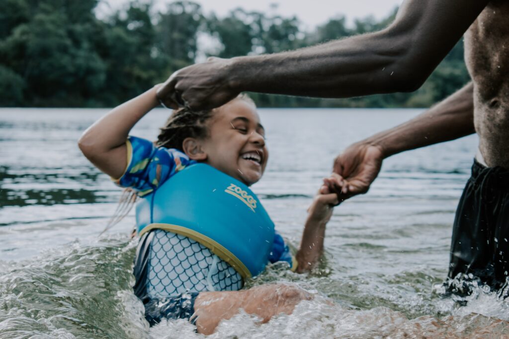Kid in the lake with her dad.  The young Black girl is wearing a life safety jacket.