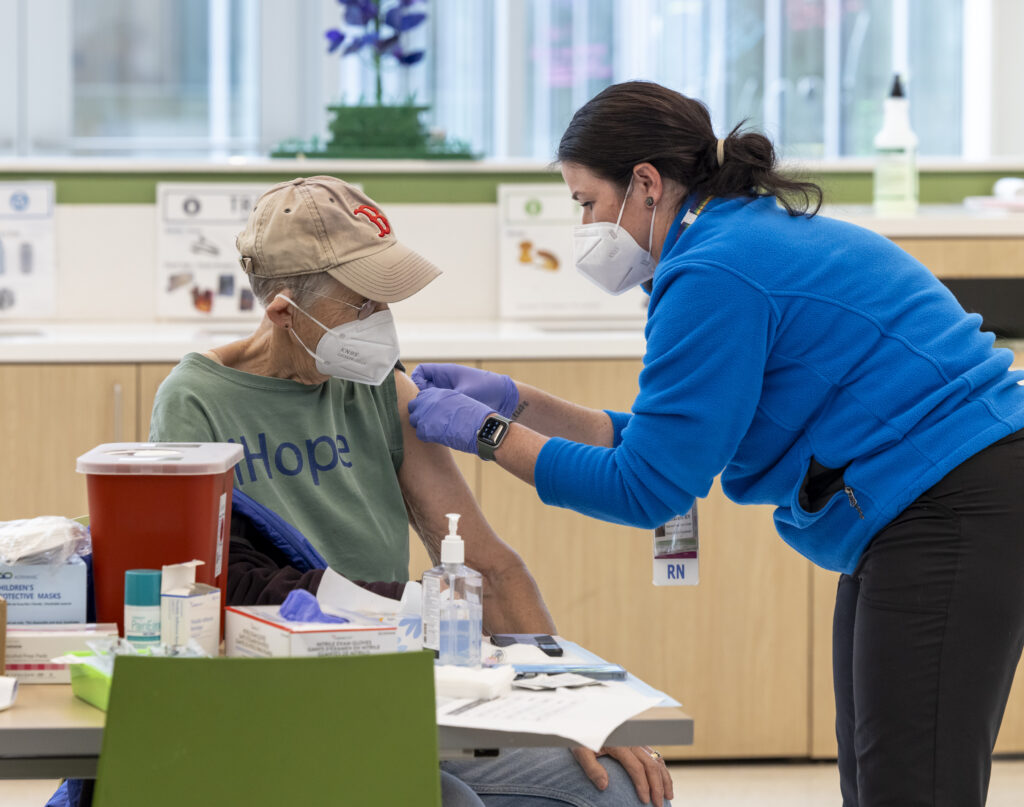 Photo of an older woman receiving a bandage from a school nurse on the spot she got the vaccine. Photo from one of CPHD's vaccine clinic 2024.