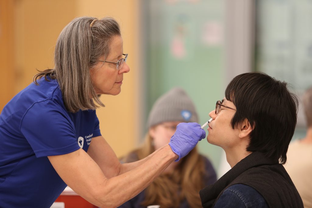 A Public Health Nurse administering a flu mist into a gentleman's nose.